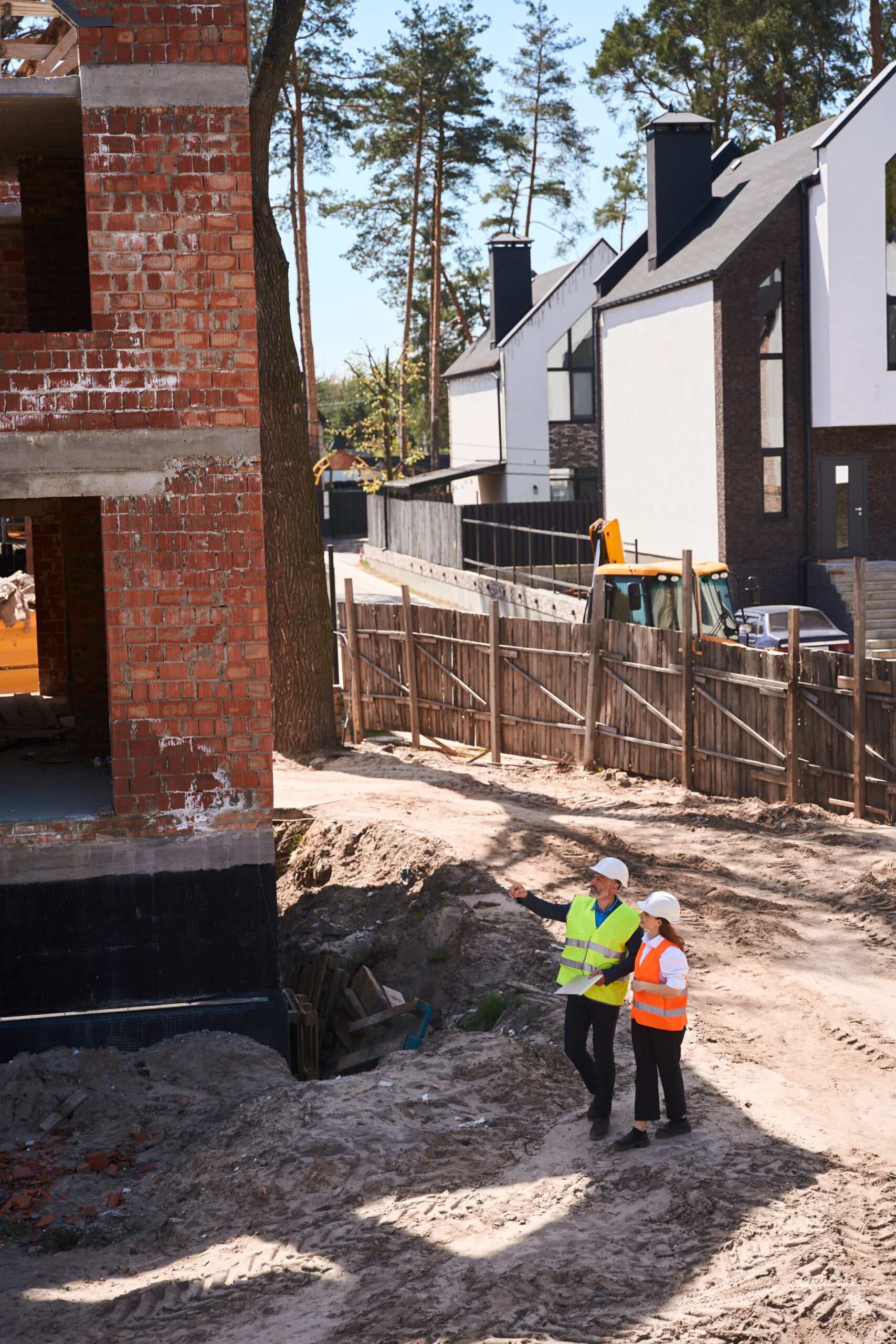 Foreman showing to female contractor in hardhat builded from bricks house, engineers discussing design and material amount, real-estate